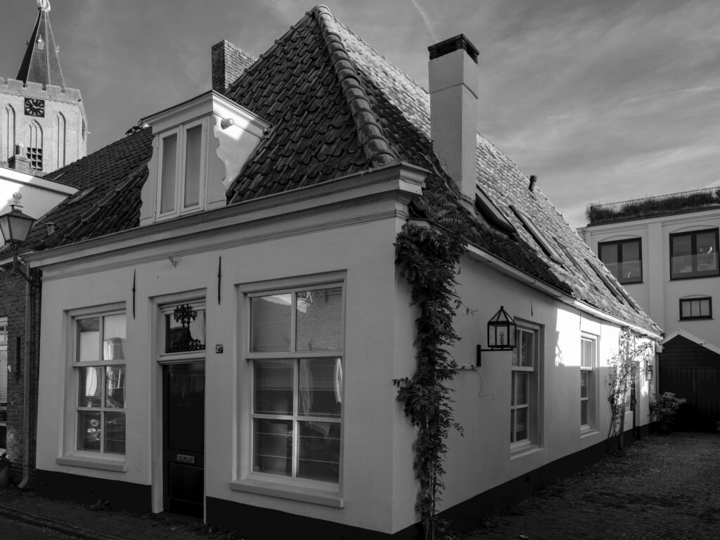 Black and white image of a charming European cottage with ivy-covered walls and steep roof.