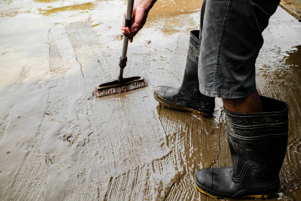 Side view of crop anonymous male worker in gumboots with brush priming cement floor at work